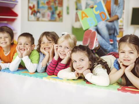 Sechs liegendene Kinder die erfreut eine Geschichte anhören.