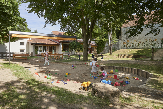 Kinder spielen im Außenbereich des Kindergartens Storchennest im Sand umgeben von einer Grünfläche