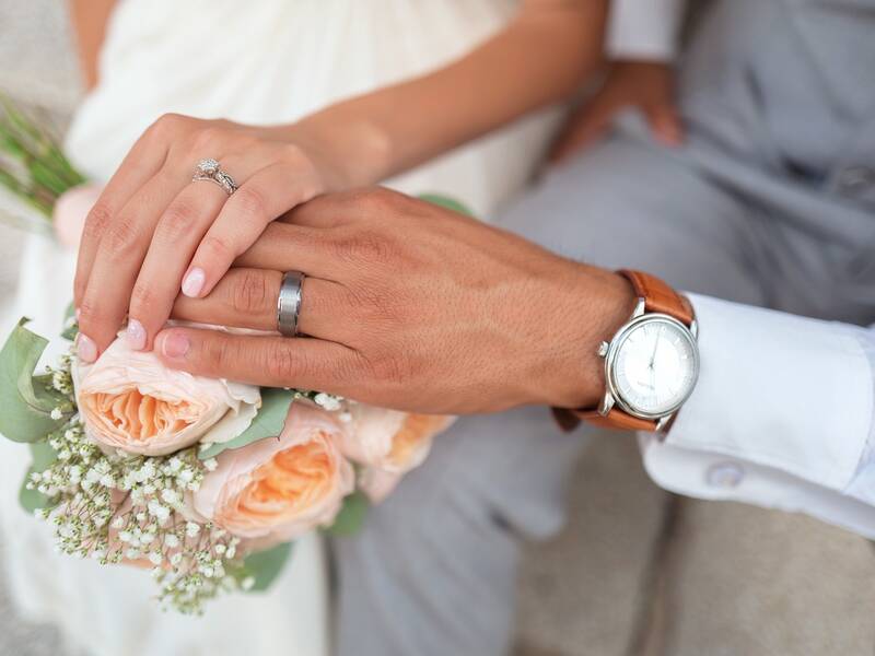 Hände von Mann und Frau mit Hochzeitsblumenstrauß