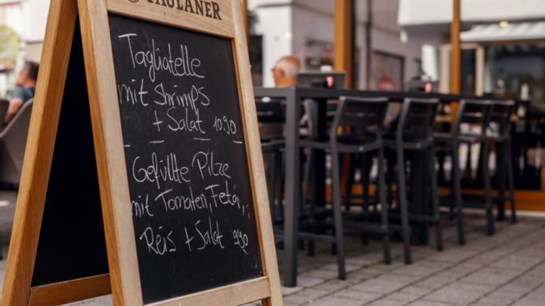 Kreidetafel auf der Straße mit Tagesmenü vor dem Plaza Cafe mit Außenbestuhlung im Hintergrund