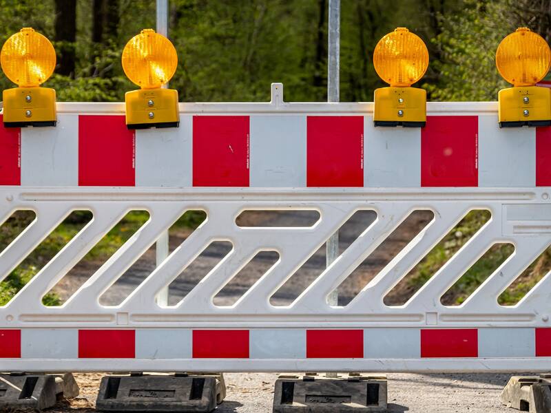 Weiß-rot gestreifte Straßensperre auf einem Weg, im Hintergrund grüne Bäume und Sträucher; Absperrung; Sperrung