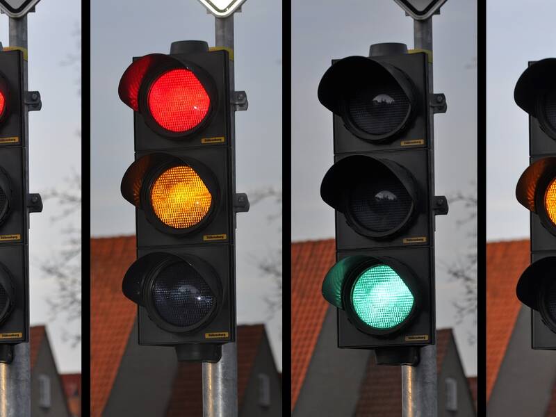 Vier Verkehrsampeln in einer Reihe zeigen verschiedene Lichtsignale: Rot, Rot-Gelb, Grün und Gelb.