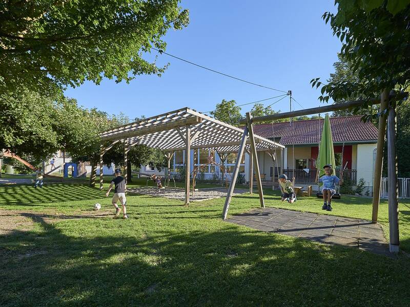 Spielende Kinder inmitten auf der Grünfläche und den Spielgeräten auf dem Außengelände des Kindergartens Pflummern