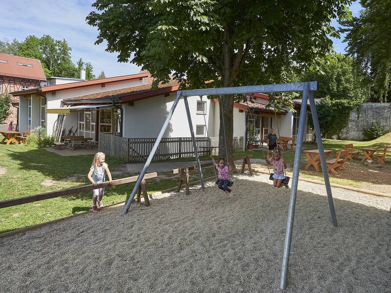 Außengelände des Kindergartens Storchennest mit spielenden Kindern auf der Schaukel