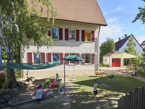 Gebäude mit Außengelände des Kindergartens Zwiefaltendorf mit Spielgeräten und spielenden Kindern