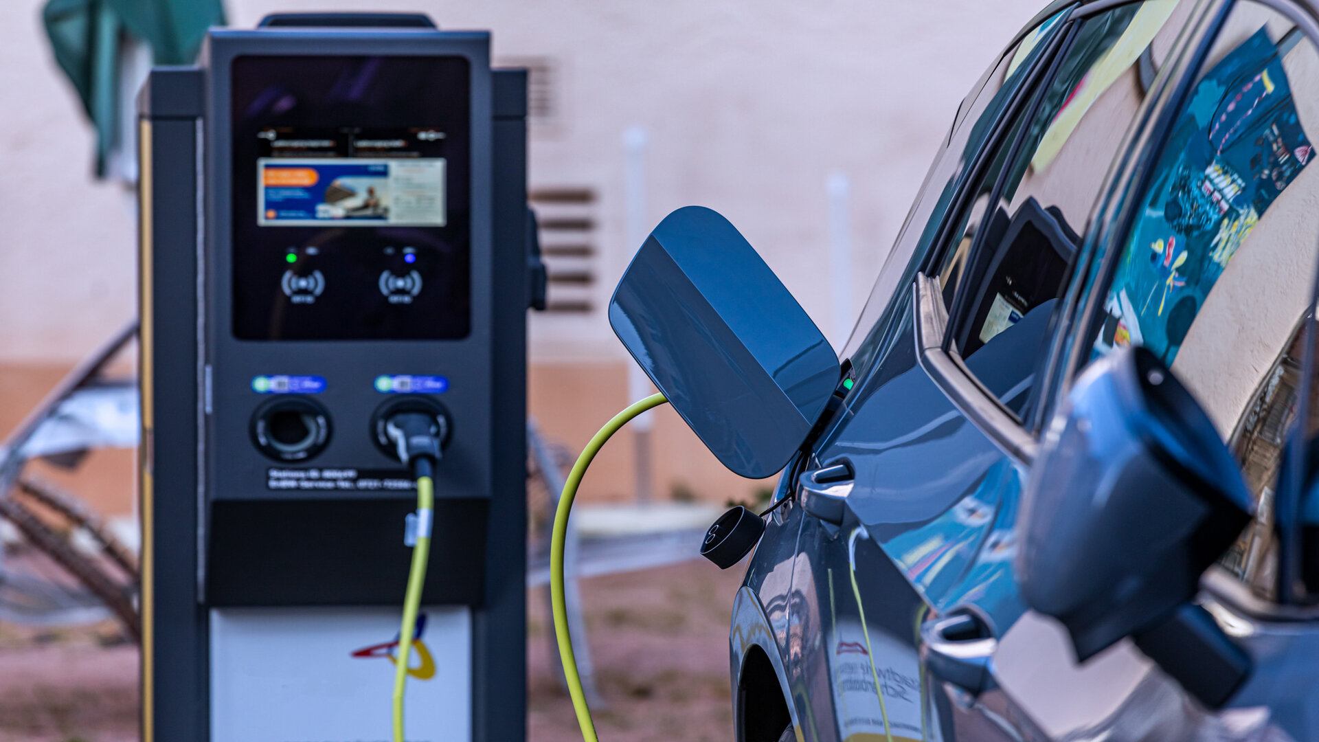 Eine E-Ladestation für Elektroautos. Von der Ladestation führt ein Ladekabel in die Tanköffnung eines grauen Autos.